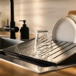 Egouttoir vaisselle design en inox noir, surface inclinée anti eau stagnante près de l’évier.